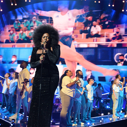 A woman in a black dress sings on stage at the national lottery homecoming event at AO arena.