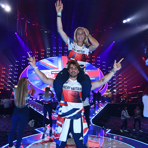 Two people with raised arms on stage, part of the national lottery Team GB homecoming event at AO Arena for Paris Olympics 2024.